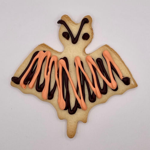 Bat-shaped cookie with orange and chocolate drizzle on a white background