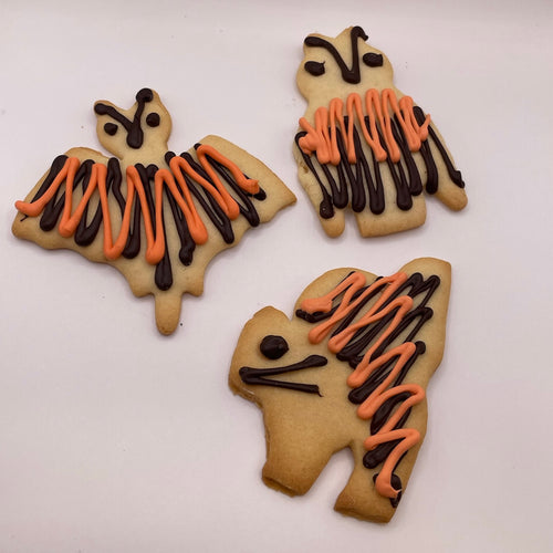 Three cookies shaped like bats,cats, and owls with orange and black icing on a white background