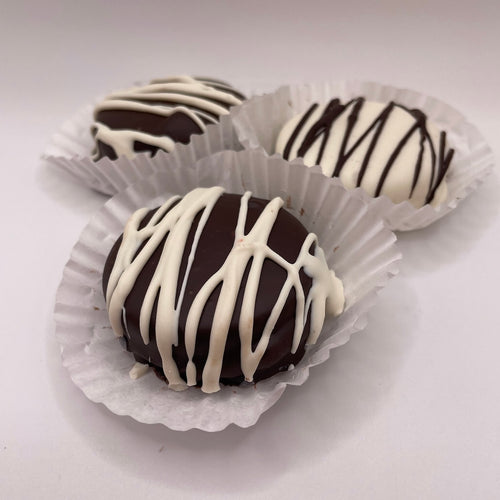 Three chocolate Oreos with white drizzle in paper cups on a white background