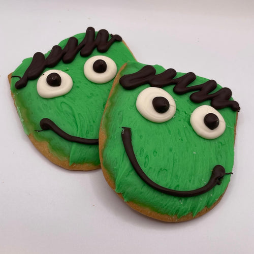 Two green cookies with black and white facial features meant to look like Frankenstein on a white background