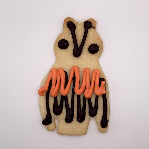 Decorative cookie shaped like an owl with orange and black icing on a white background